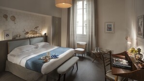A hotel room with a large bed, a desk with a magazine, a chair, and a window with curtains. - Alfieri9 (Florence)