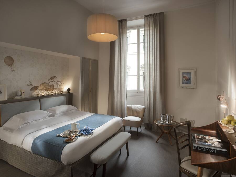 Een hotelkamer met een groot bed, een bureau met een tijdschrift, een stoel en een raam met gordijnen.
