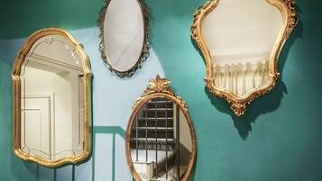 A room with teal walls, three ornate mirrors, a wooden table with candles, and a green vase.