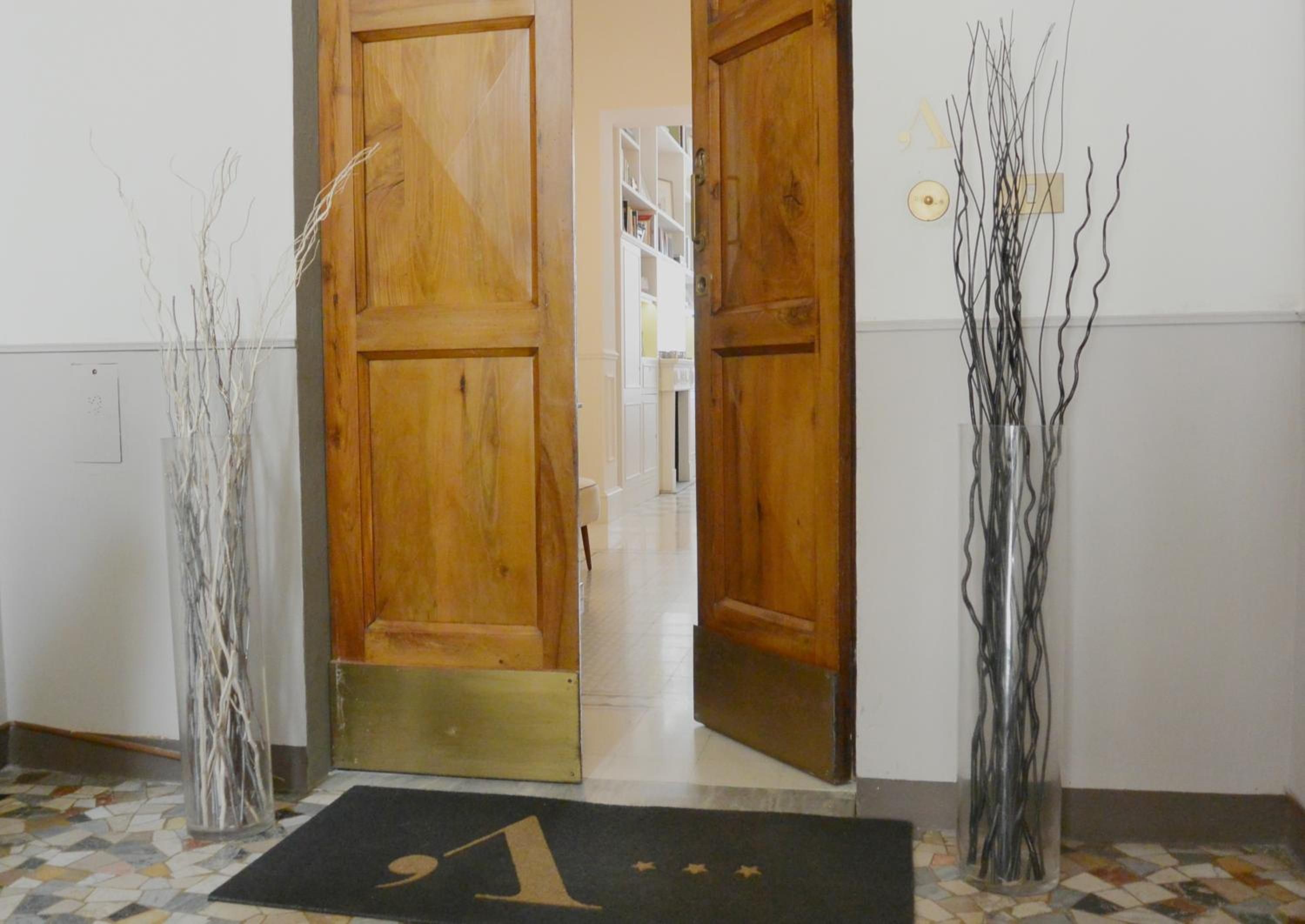 A hallway with wooden doors, a doormat with a number, and two tall vases with branches.