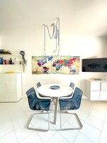 Et spiseområde med et hvidt bord og blå stole, et verdenskort som kunst på væggen, og et fjernsyn til højre.