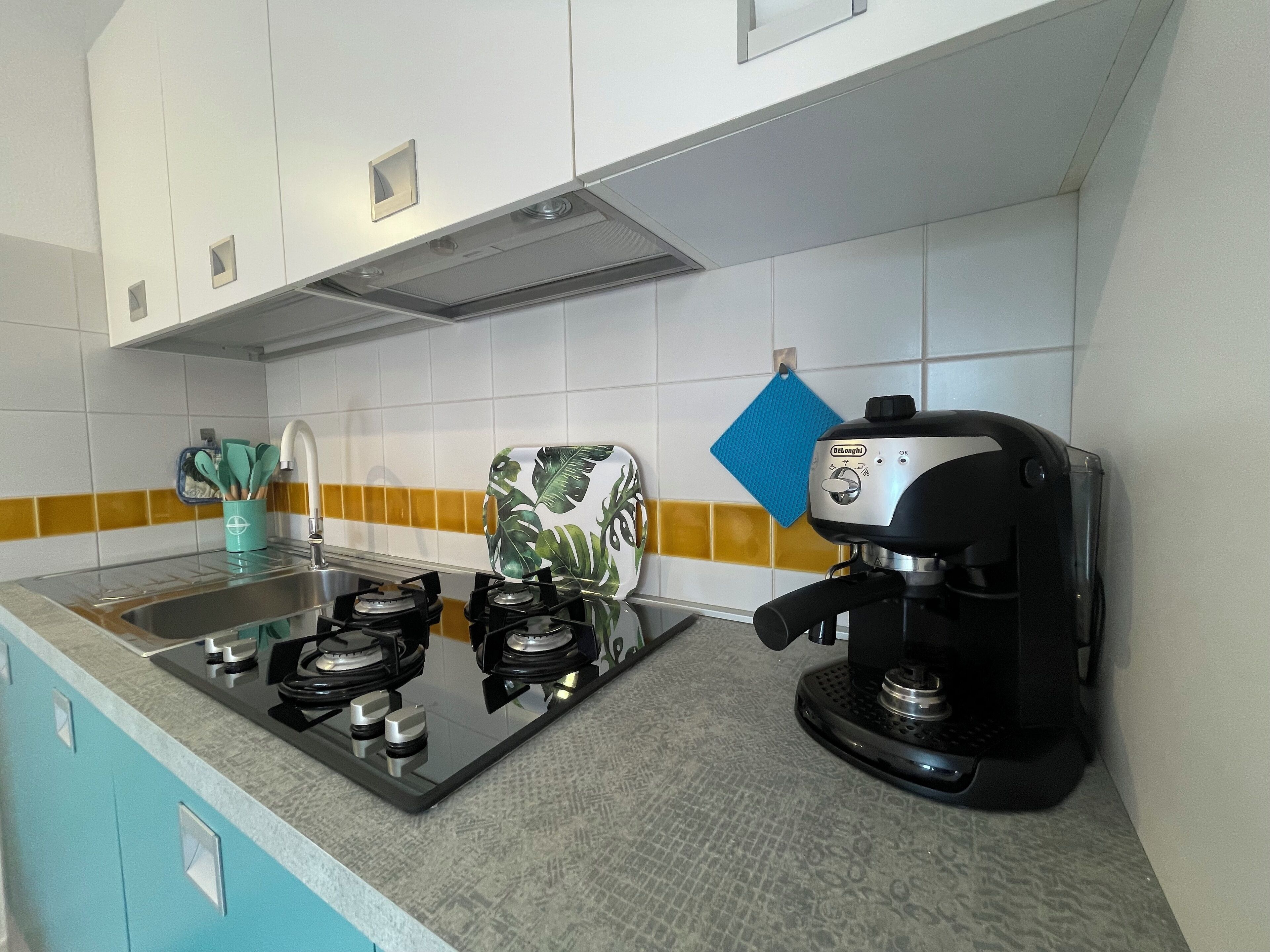 Une cuisine équipée d’une cuisinière à gaz, d’une machine à café et d’un torchon bleu accroché au mur.