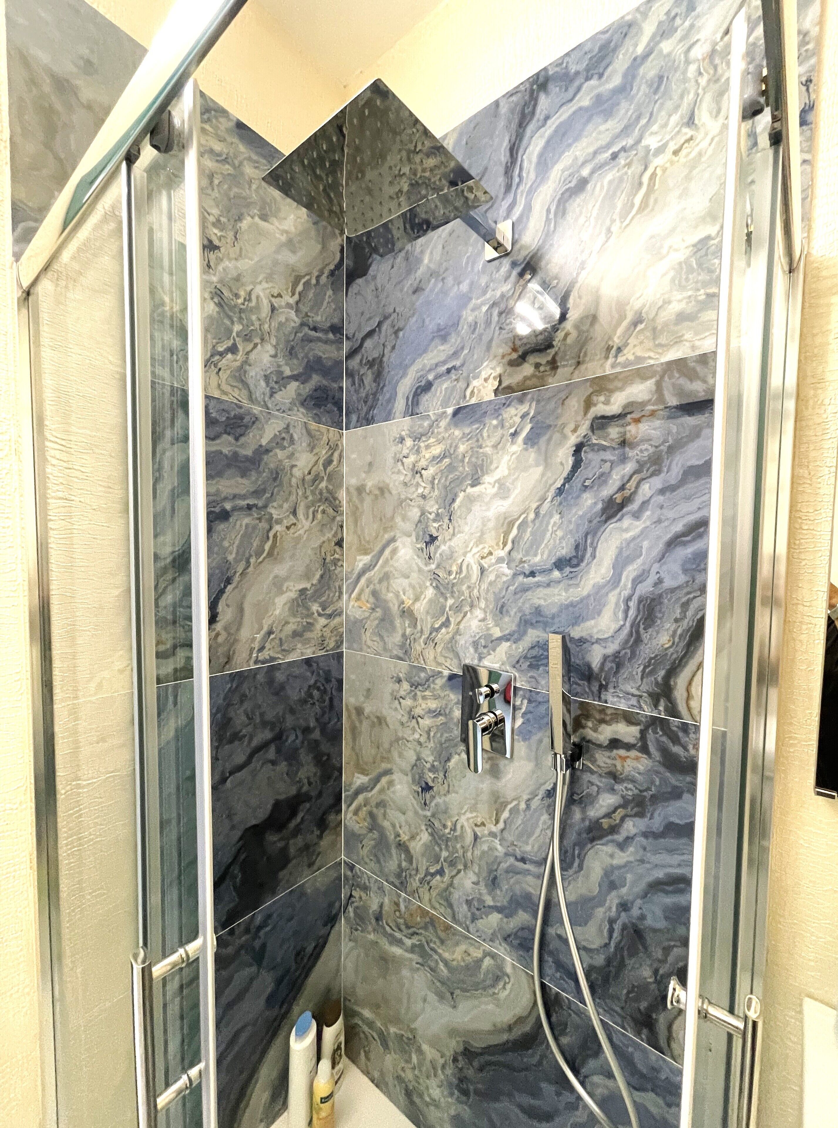 Una ducha con puerta de cristal y pared de mármol.