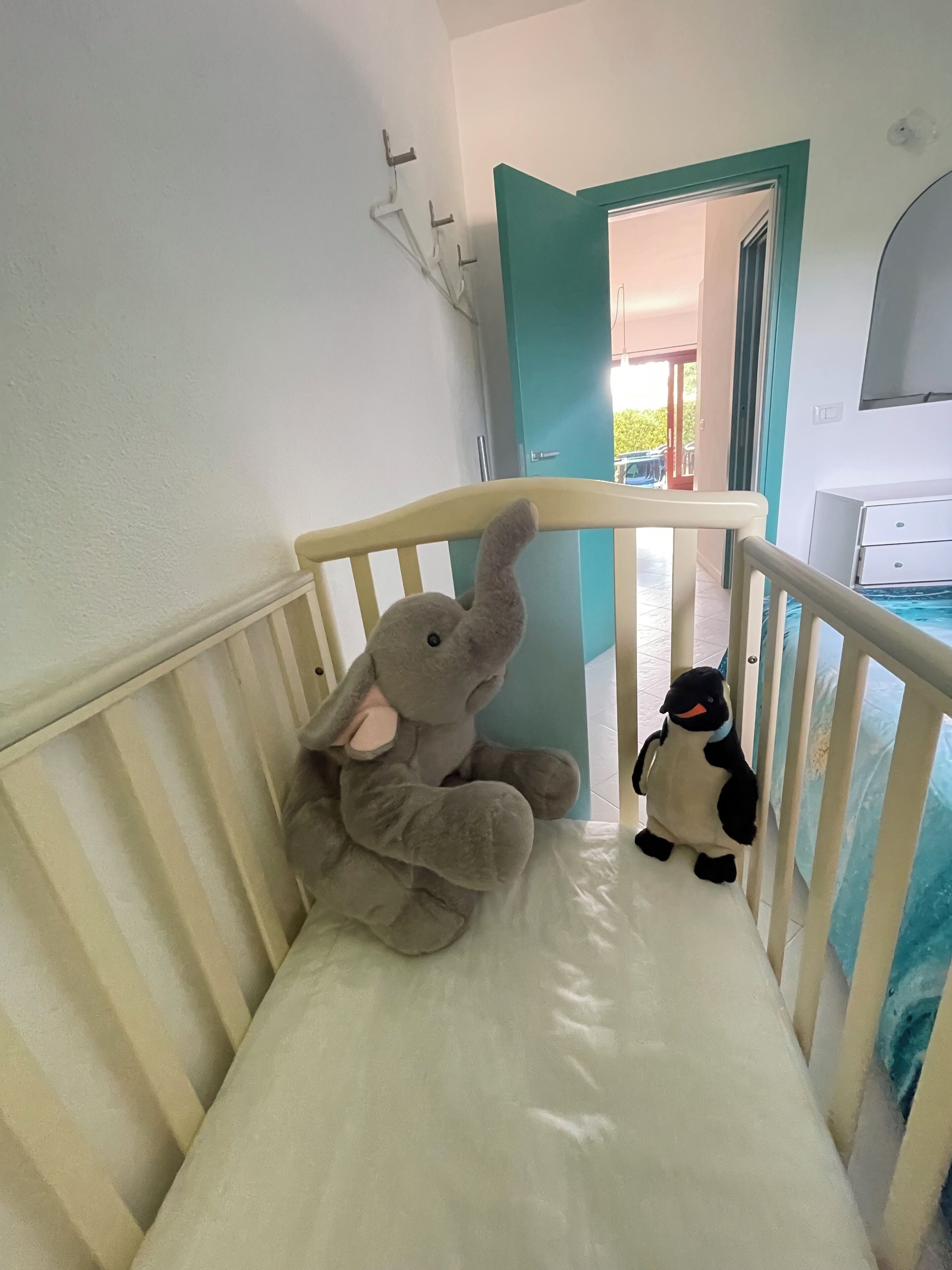Un berceau avec un matelas blanc, un doudou en forme d’éléphant gris et un doudou en forme de pingouin.