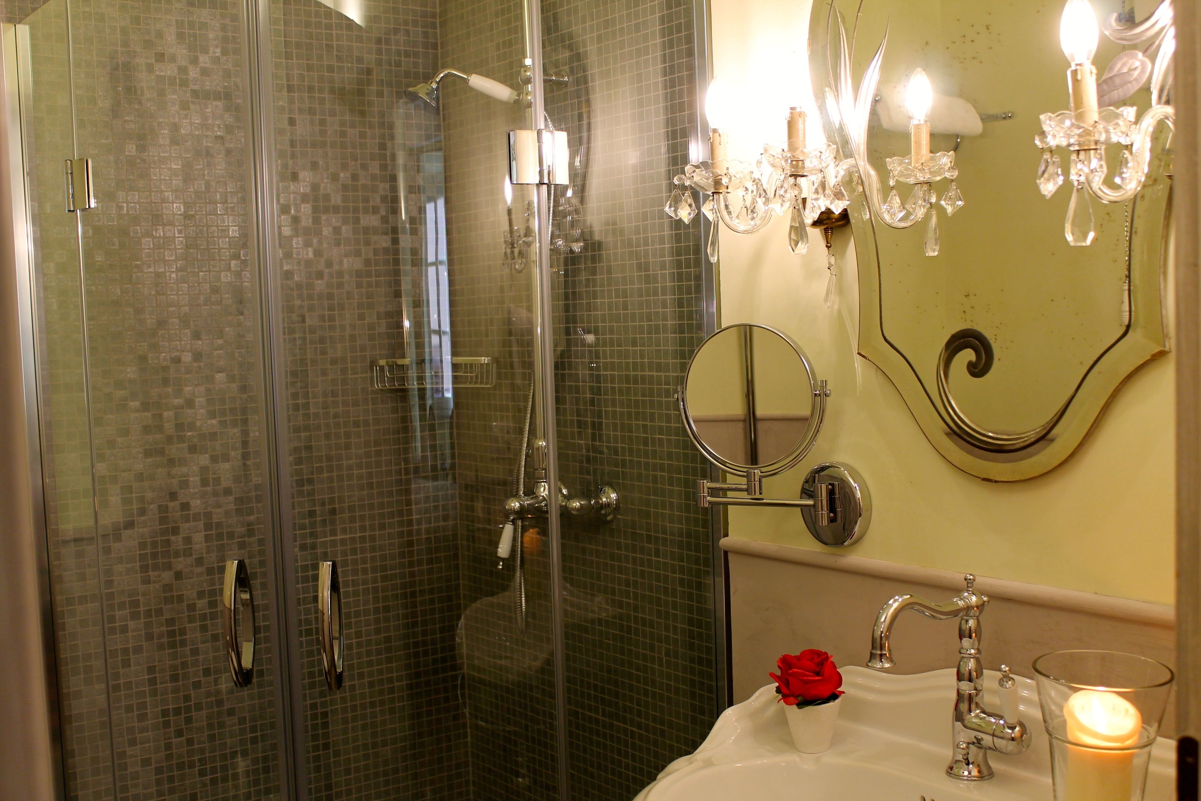 A bathroom with a glass-enclosed shower, a sink with a mirror, and wall-mounted lighting.