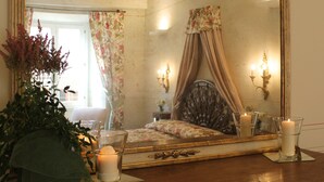 Quarto com um espelho grande e ornamentado, cortinas florais, cama com dossel e duas velas fixadas na parede.