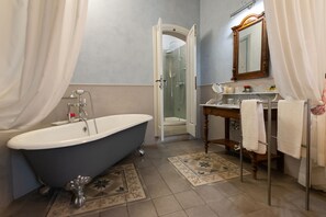 Un baño con bañera de patas de león, ducha con mampara de vidrio, tocador de madera con espejo y perchero para toallas.