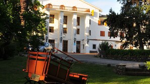 A white building with a balcony, surrounded by greenery and a horse-drawn carriage.
