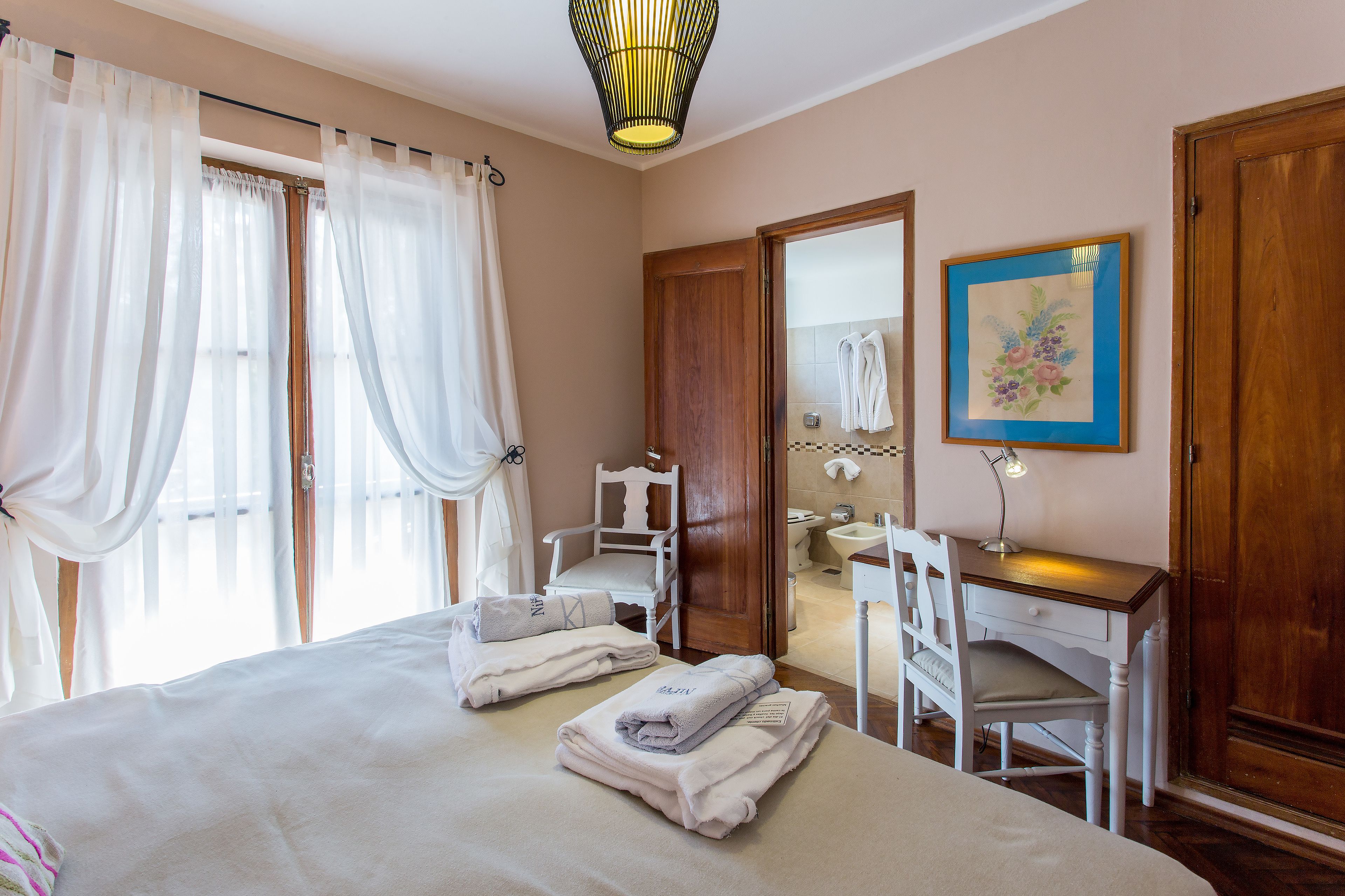 A hotel room with a bed, a desk, a chair, a bathroom, and a painting on the wall.