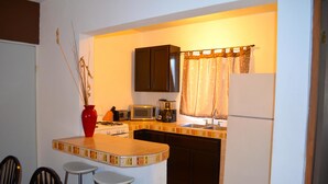 A compact kitchen with a microwave, toaster, and coffee maker. There are three stools and a small island with a red vase. - Las Glorias LG104 1 Bedroom Apartment By Seaside San Carlos (San Carlos)