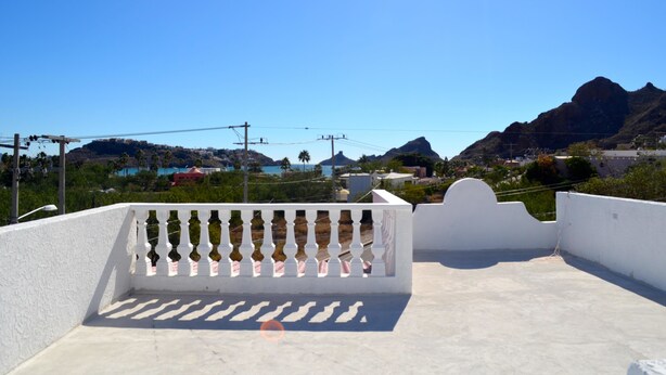 A rooftop terrace with a white balustrade, offering a view of a mountainous landscape and a coastal area. - Las Glorias LG104 1 Bedroom Apartment By Seaside San Carlos (San Carlos)