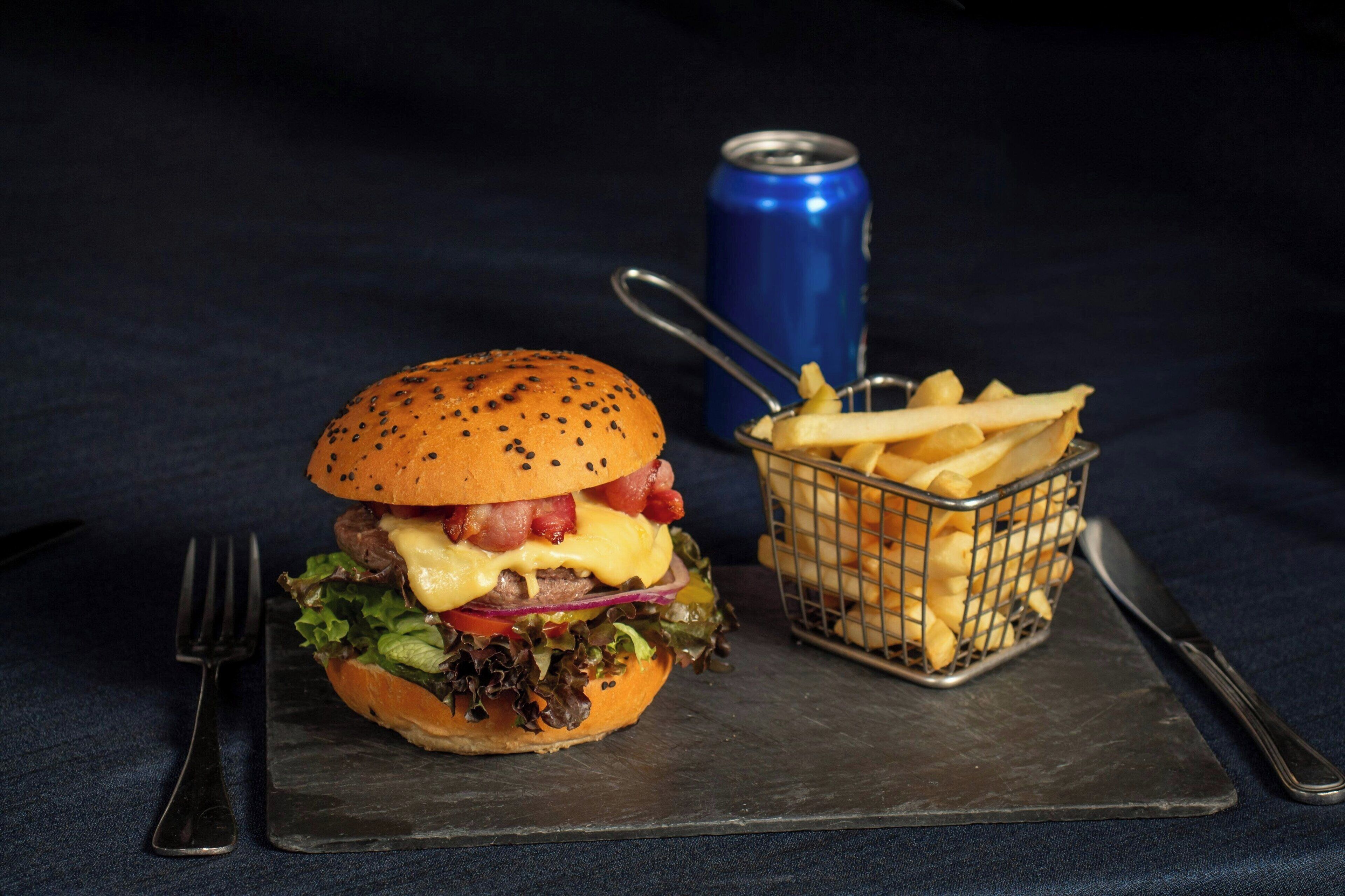 Hamburguesa con papas fritas y una lata de refresco sobre una tabla de pizarra.