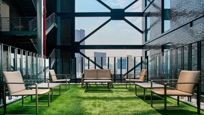 Un espace intérieur moderne, doté d’une pelouse artificielle verte, de chaises à structure métallique et offrant une vue sur le paysage urbain grâce à une grande fenêtre.