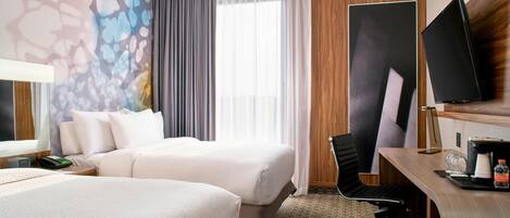 A hotel room with two beds, a desk with a computer, a flat-screen TV, and a large window with curtains.