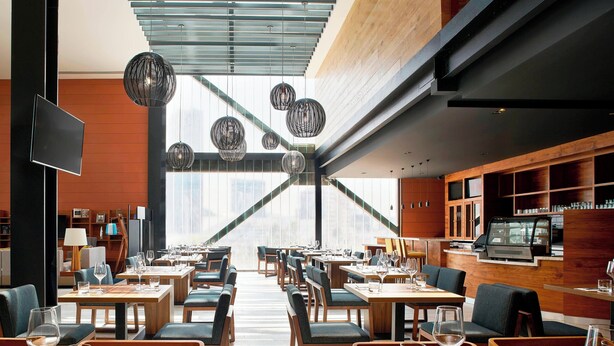 Un restaurant moderne avec des tables et des chaises en bois, des luminaires sphériques suspendus et une grande fenêtre offrant une vue sur la ville.