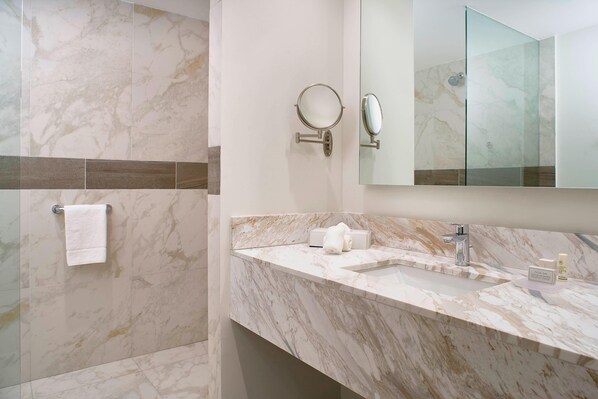 Un baño moderno con baldosas de mármol, cabina de ducha de vidrio, lavamanos con espejo y un perchero para toallas.