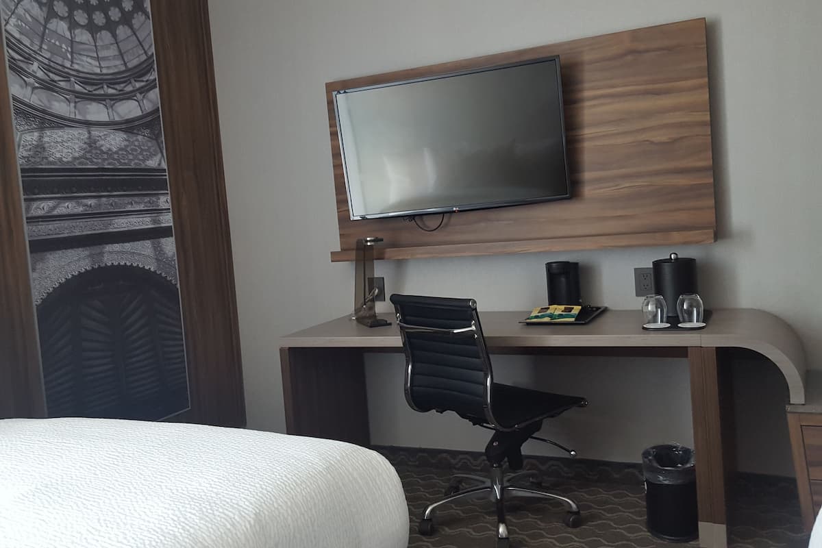 Ein Hotelzimmer mit Bett, Schreibtisch mit Stuhl, Flachbildfernseher, Kaffeemaschine und Mülleimer.