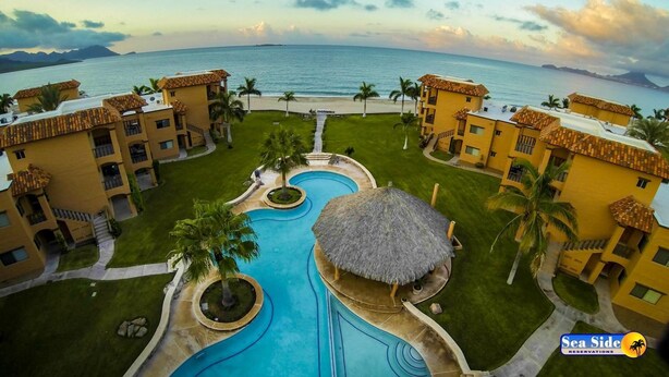 A resort with a central swimming pool, palm trees, and a view of the ocean. - Las Glorias LG307 3 Bedroom Apartment By Seaside San Carlos (San Carlos)