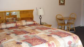 Una habitación de hotel con una cama grande, una mesita de noche con lámpara, una silla, una pequeña mesa y un cuadro en la pared.