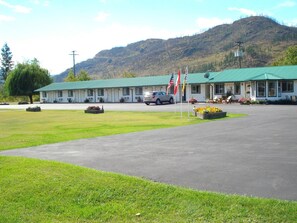 A motel with a green roof, a parking lot, and a mountainous backdrop. - Mountain Springs Motel & RV Park (Barriere)