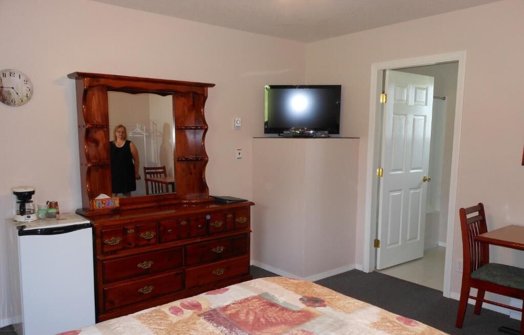 A bedroom with a wooden dresser, a television mounted on the wall, a bed with a quilt, a small desk, and a chair.