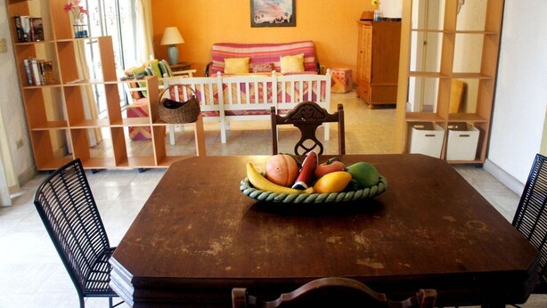 A dining area with a wooden table, chairs, and a fruit basket. There is a sofa and a bookshelf in the background. - Bahia 189 Bottom Chip s Place 1 Bedroom Apartment By Seaside San Carlos (San Carlos)