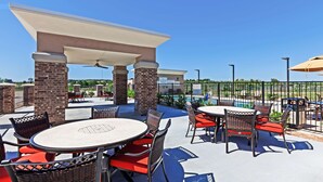 An outdoor patio area with round tables and wicker chairs, a covered seating area, and a view of a swimming pool. - Hampton Inn Ozona (Ozona)