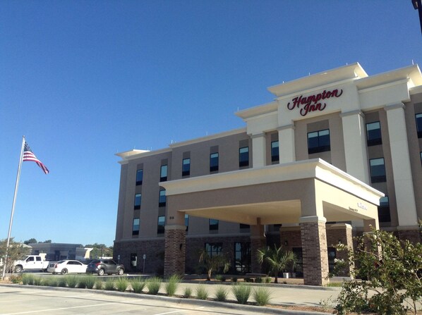 Un hotel Hampton Inn de diseño moderno, con una entrada destacada y un asta con la bandera estadounidense.