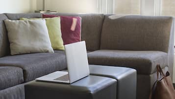 Un salon moderne avec un canapé d’angle, un petit pouf, un ordinateur portable et une paire de chaussures posées sur le sol.
