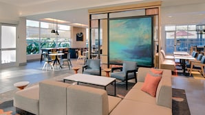 A modern lounge area with sofas, tables, and chairs, large windows with a city view, and a large abstract painting on the wall.