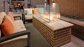 An outdoor seating area with wicker furniture, a glass-top fire feature, and a brick wall backdrop. - Hyatt House Irvine/John Wayne Airport (Irvine)