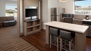 A modern kitchen with a built-in refrigerator, microwave, and coffee maker, a dining area with bar stools, and a large window offering a city view.