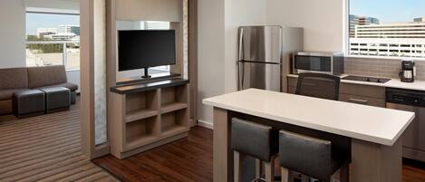 A modern kitchen with a built-in refrigerator, microwave, and coffee maker, a dining area with bar stools, and a large window offering a city view.