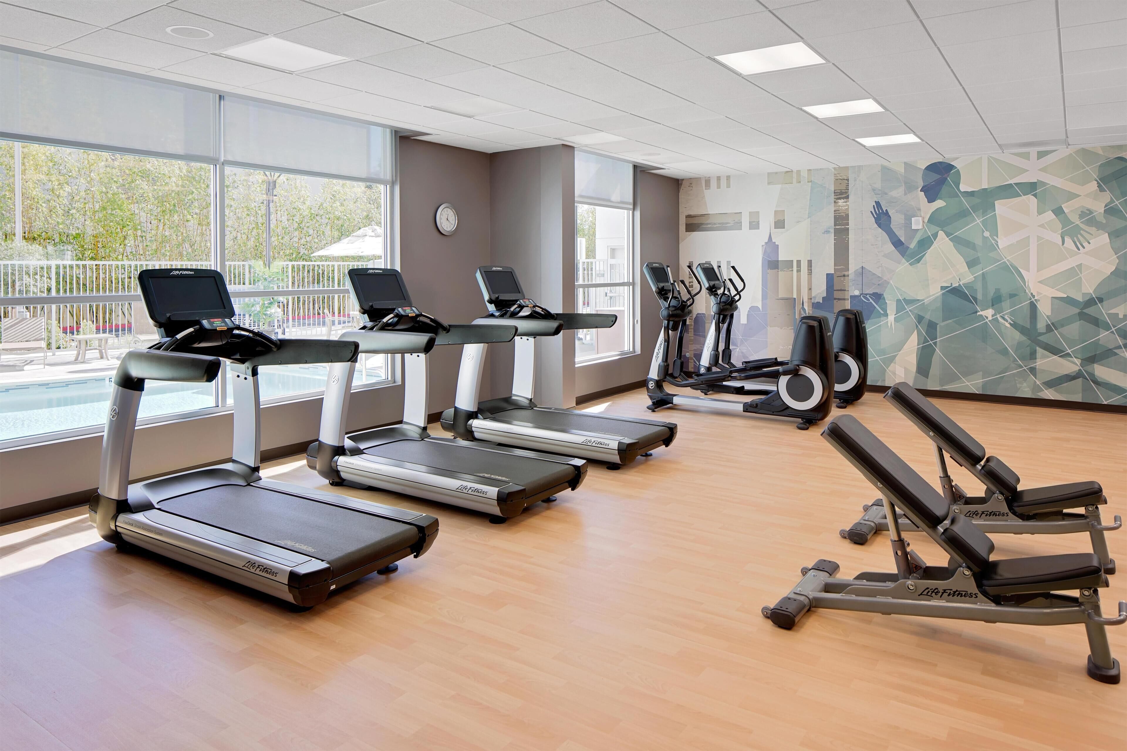 Une salle de sport équipée de tapis de course, d’un banc de développé couché et de grandes fenêtres.