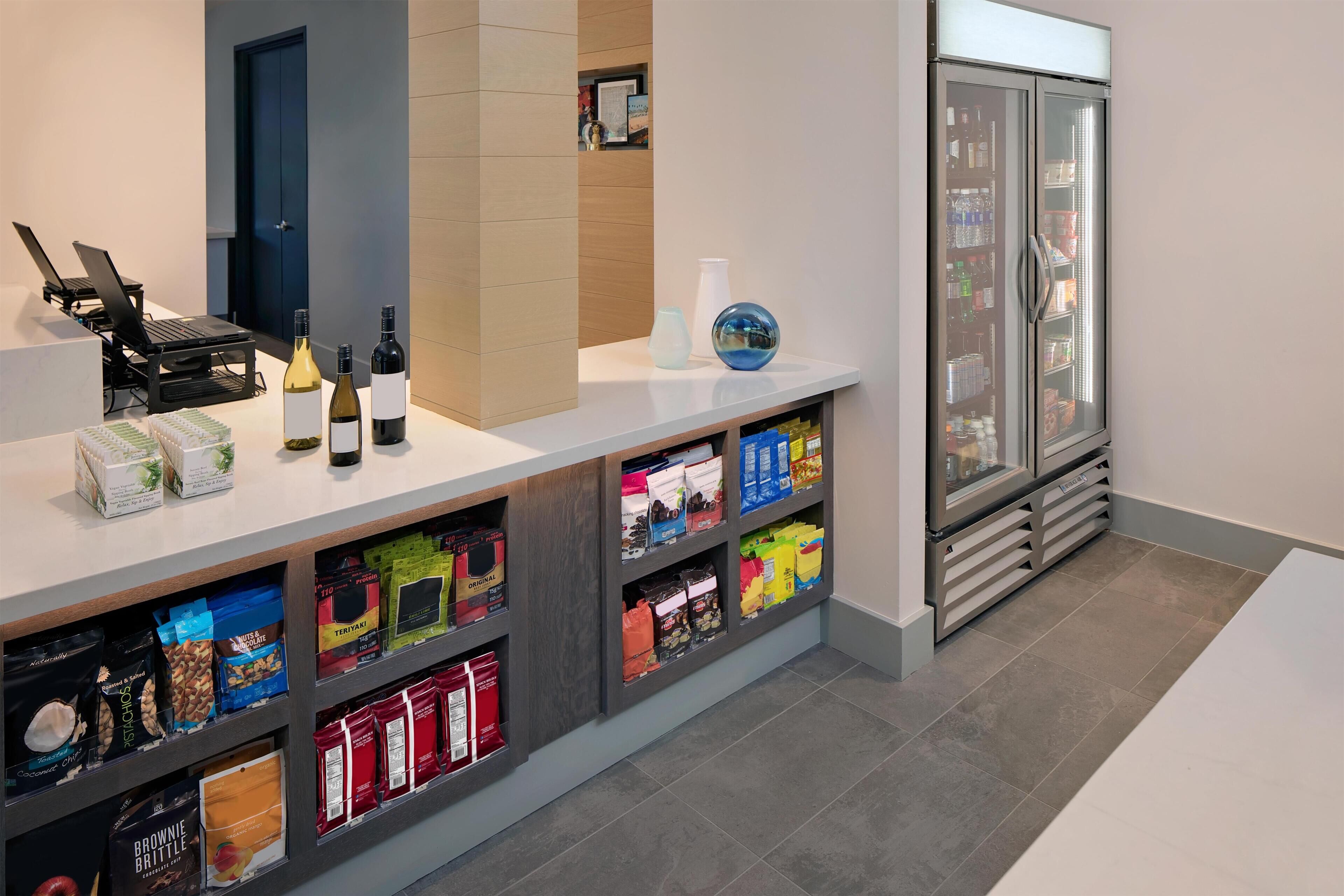 A hotel reception area with a counter, laptops, wine bottles, and a refrigerator stocked with beverages.