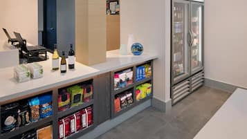 A hotel reception area with a counter, laptops, wine bottles, and a refrigerator stocked with beverages.