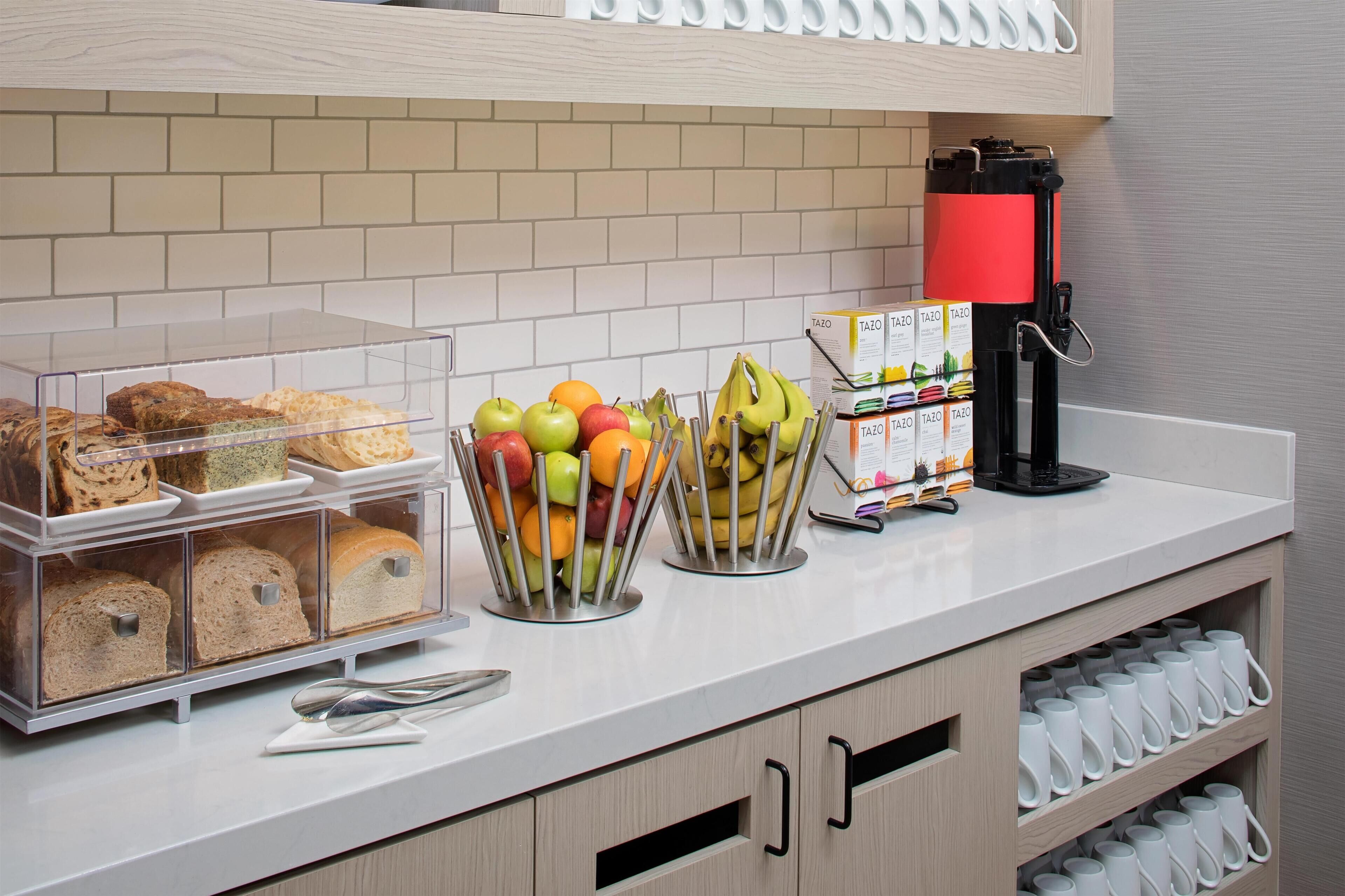 A breakfast bar with clear storage containers holding bread, a fruit basket, and a coffee machine.