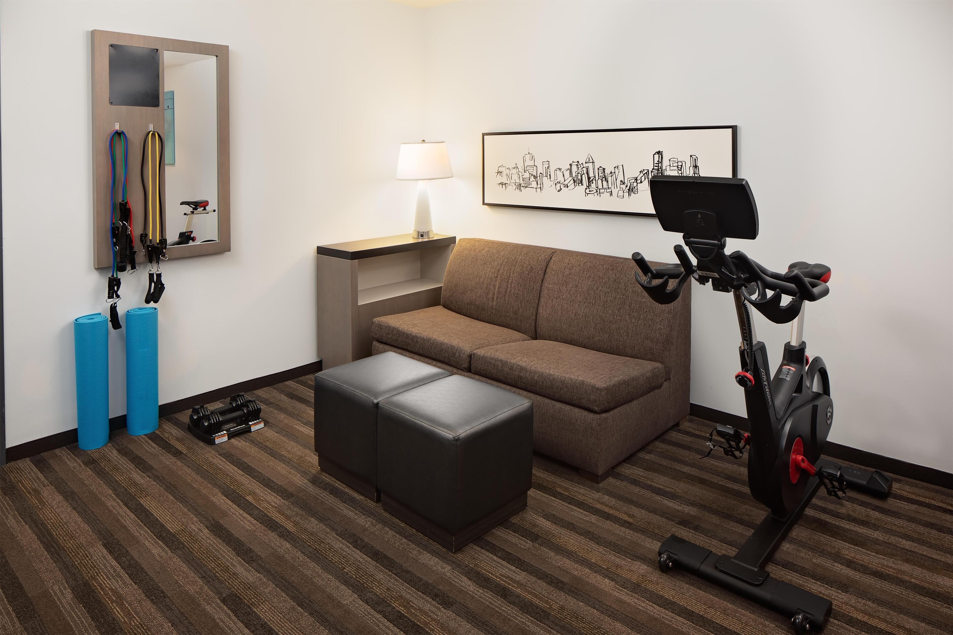 Una habitación con una bicicleta estática, un sofá, un espejo, una lámpara y equipo de ejercicio.