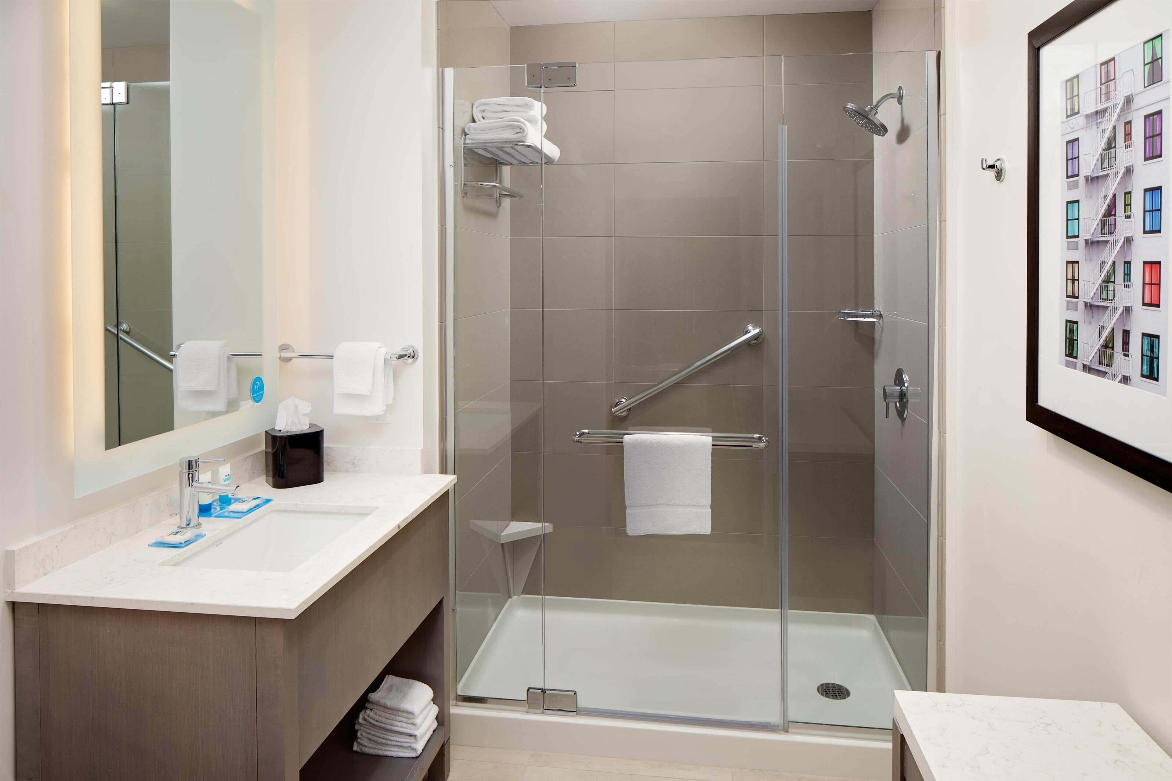 A modern bathroom with a glass-enclosed shower, a sink with a marble countertop, and a framed picture on the wall.
