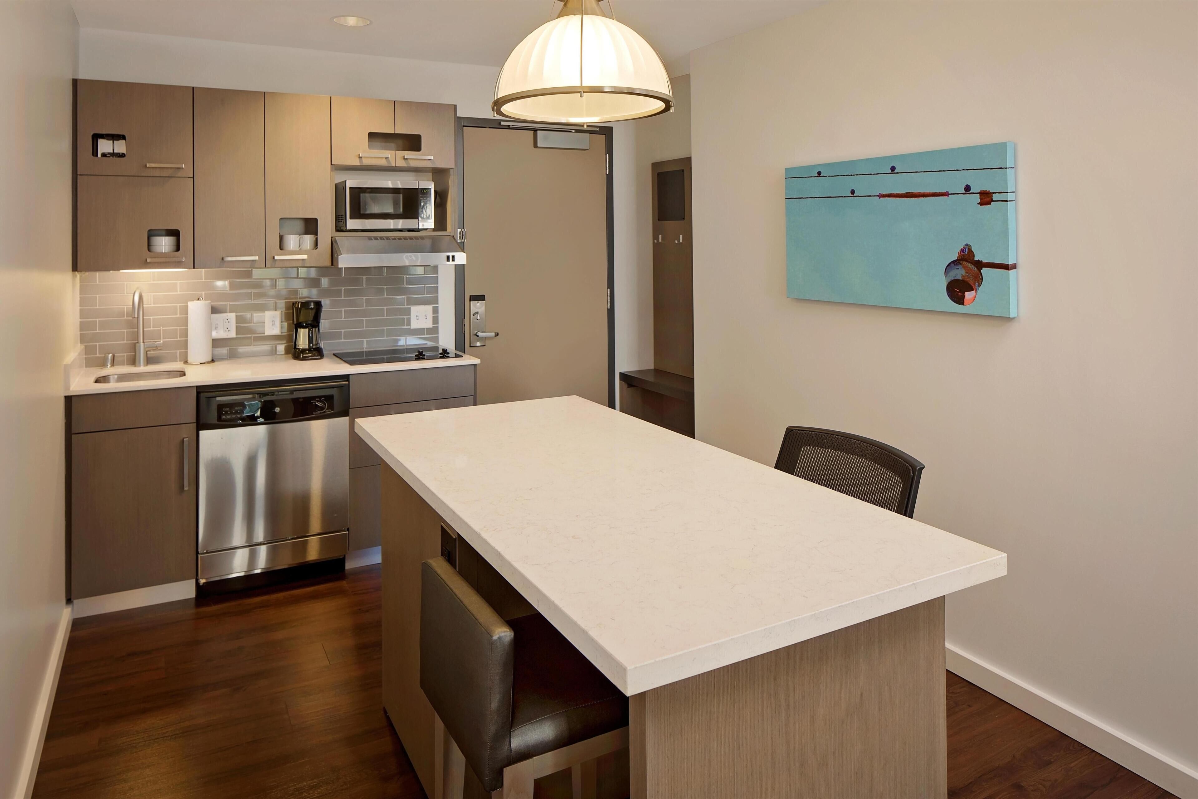 A modern kitchen with stainless steel appliances, a white countertop, and a hanging light fixture.