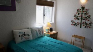 A bedroom with a teal bedspread, a nightstand with a lamp, and a wall decoration. - Caracol Peninsula 544 A 2 Bedroom Apartment By Seaside San Carlos (San Carlos)