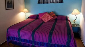 Een bed met een gestreept dekbedovertrek, twee bedlampjes, een raam met gordijn en een ingelijst schilderij aan de muur.