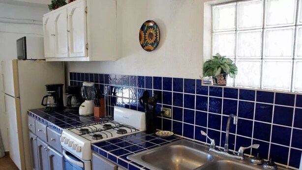 Een keuken met witte kasten, een fornuis, een spoelbak en een blauwe tegelachtergrond.