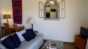 Een woonkamer met een bank, een glazen salontafel, een tv-meubel, een spiegel, een lamp, een stoel en een tapijt met een patroon.
