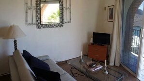 Een woonkamer met een bank, een glazen salontafel, een televisie op een houten kast en een grote spiegel met een sierlijk lijstwerk.