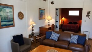 Sala de estar com sofá de couro marrom, poltrona cinza e mesa de centro de madeira. Há um quadro na parede e um abajur sobre a mesa.