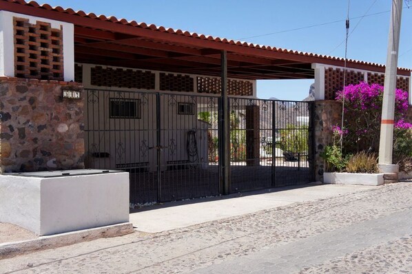 Una entrada protegida por un muro de piedra, una reja metálica y un porche con techo rojo.