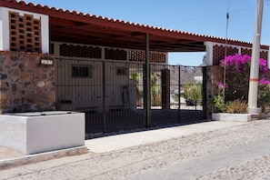 Una entrada protegida por un muro de piedra, una reja metálica y un porche con techo rojo.