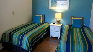 A room with two beds, each with striped bedding, a nightstand with a lamp, and a framed picture on the wall.