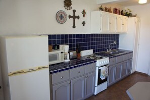 Een keuken met witte kastjes, een fornuis, een spoelbak en een magnetron.